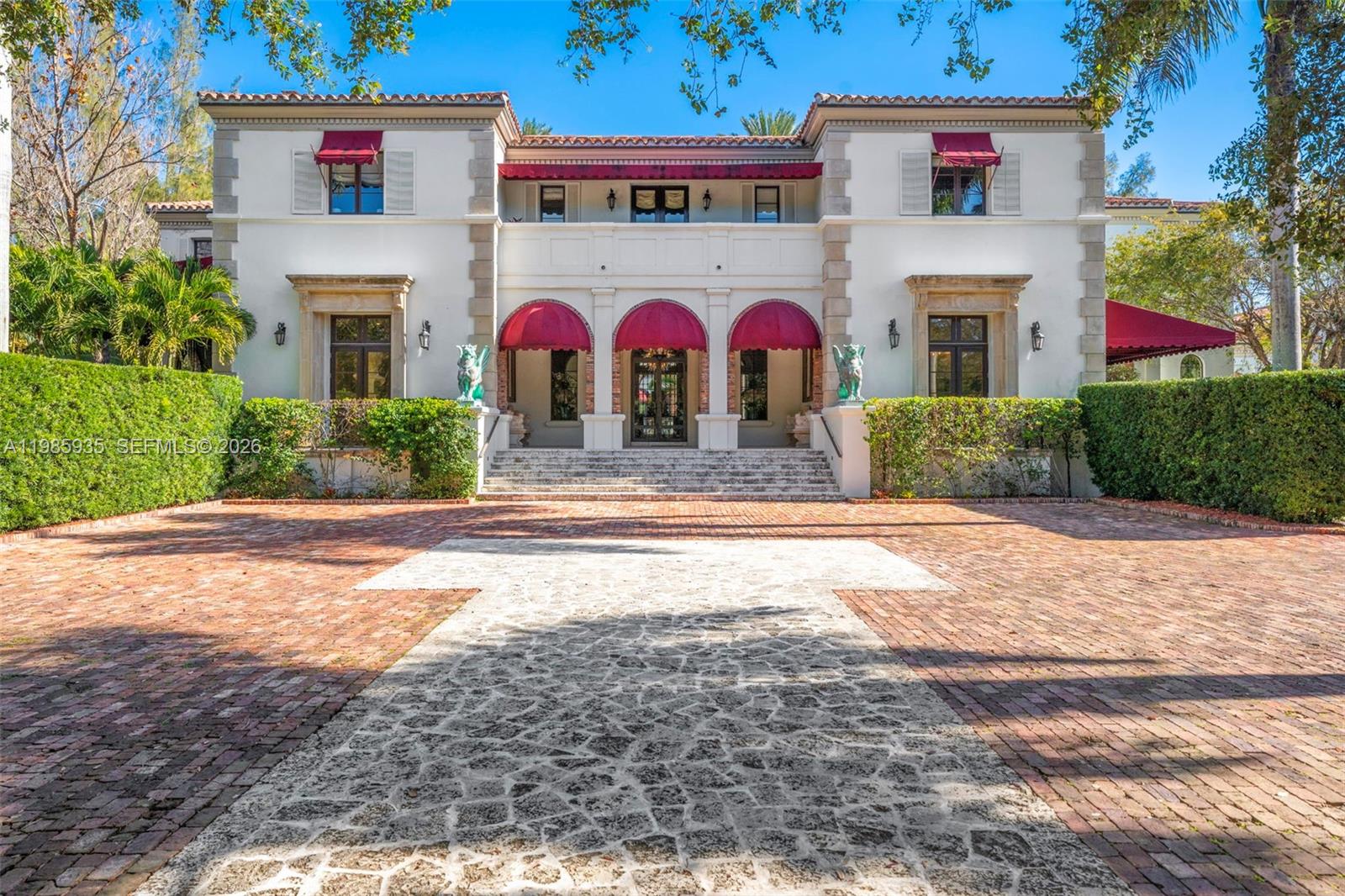 A two-story Mediterranean-style mansion features a brick driveway, red awnings, and stone stairs — 9401 Journeys End Rd, Coral Gables FL 33156, CORAL GABLES, FL