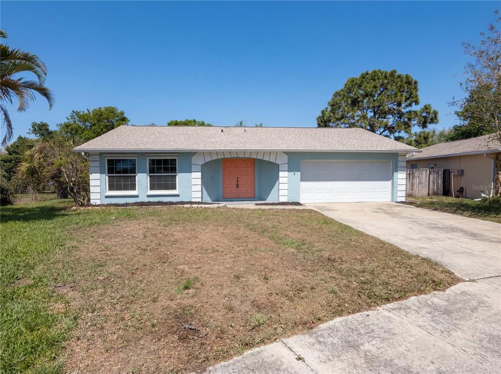 A single-story house with light blue siding, a white garage door, and a coral front door — 1512 CASCADE COURT, DUNEDIN, FL
