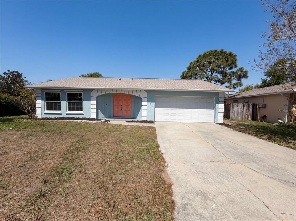 A light blue single-story house features a white garage door and a bright orange front door — 1512 CASCADE COURT, DUNEDIN, FL