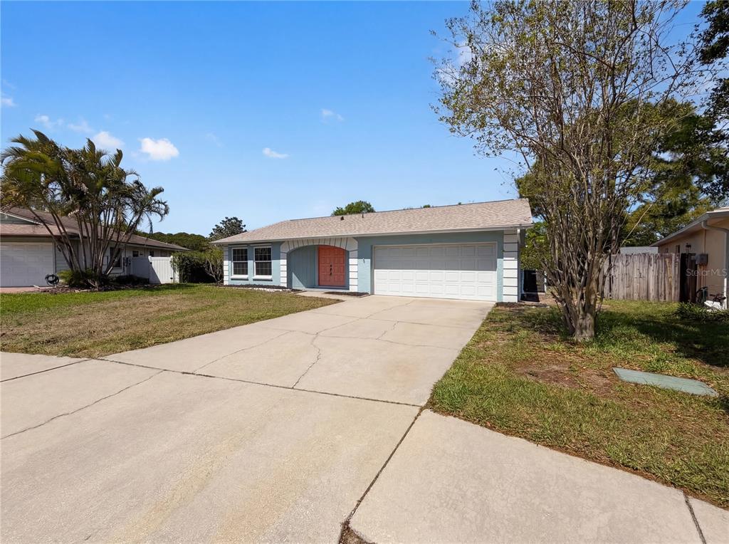A single-story house with a light blue exterior, a white garage door, and a coral-colored door — 1512 CASCADE COURT, DUNEDIN, FL