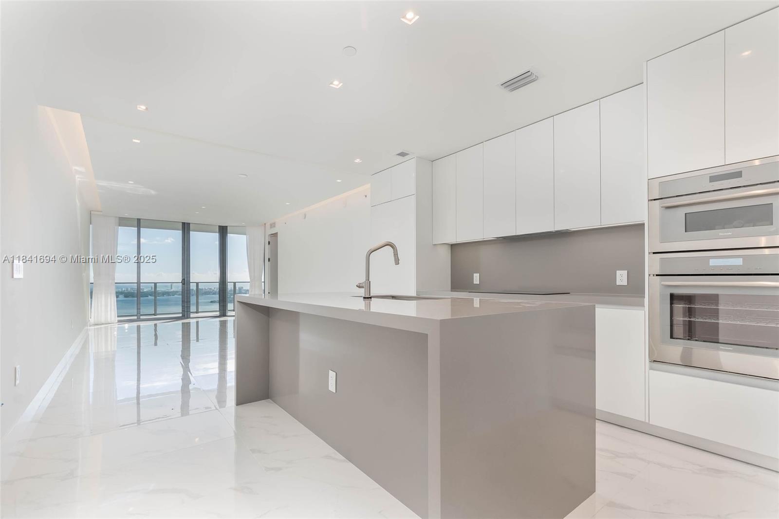A modern kitchen features a large gray island, white cabinetry, and floor-to-ceiling windows with water views — 700 NE 24 ST # 5005, Miami FL 33137, MIAMI, FL