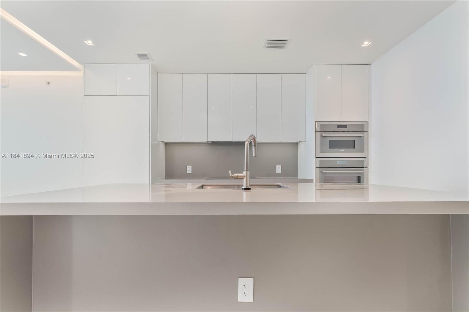 A modern kitchen features white cabinetry, a gray backsplash, stainless steel appliances, and a countertop — 700 NE 24 ST # 5005, Miami FL 33137, MIAMI, FL