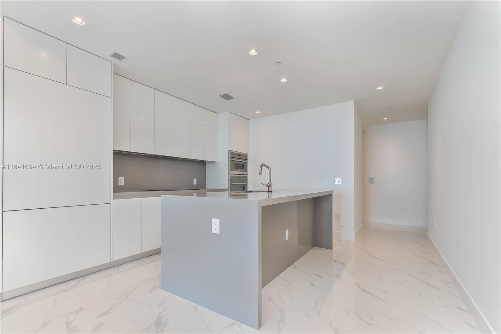 A modern kitchen features white cabinetry, a gray island with a sink, and marble flooring — 700 NE 24 ST # 5005, Miami FL 33137, MIAMI, FL