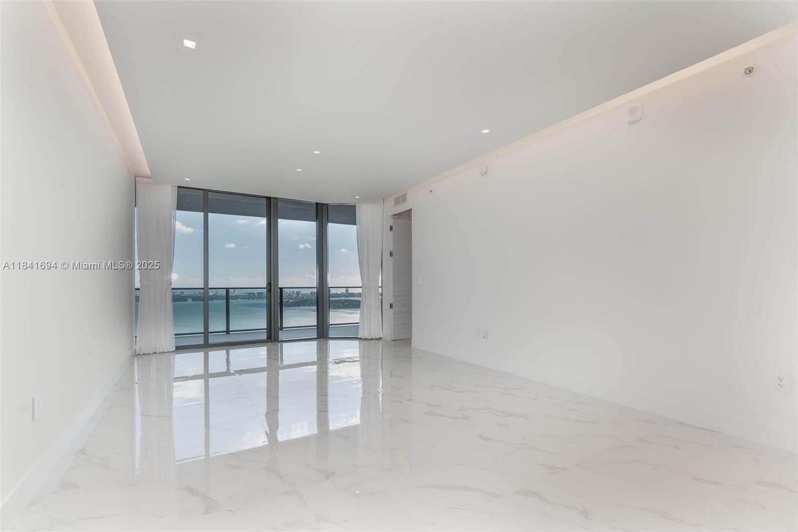 An empty room with white marble floors, recessed lighting, and floor-to-ceiling windows overlooking the water — 700 NE 24 ST # 5005, Miami FL 33137, MIAMI, FL