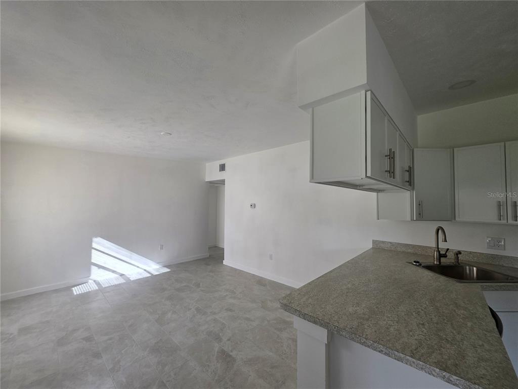 A kitchen with white cabinets and granite countertops overlooks an open, tiled living area — 219 HAYS DRIVE, SANFORD, FL