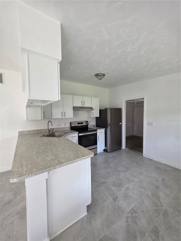 A kitchen features white cabinets, stainless steel appliances, gray countertops, and light gray tile flooring — 219 HAYS DRIVE, SANFORD, FL