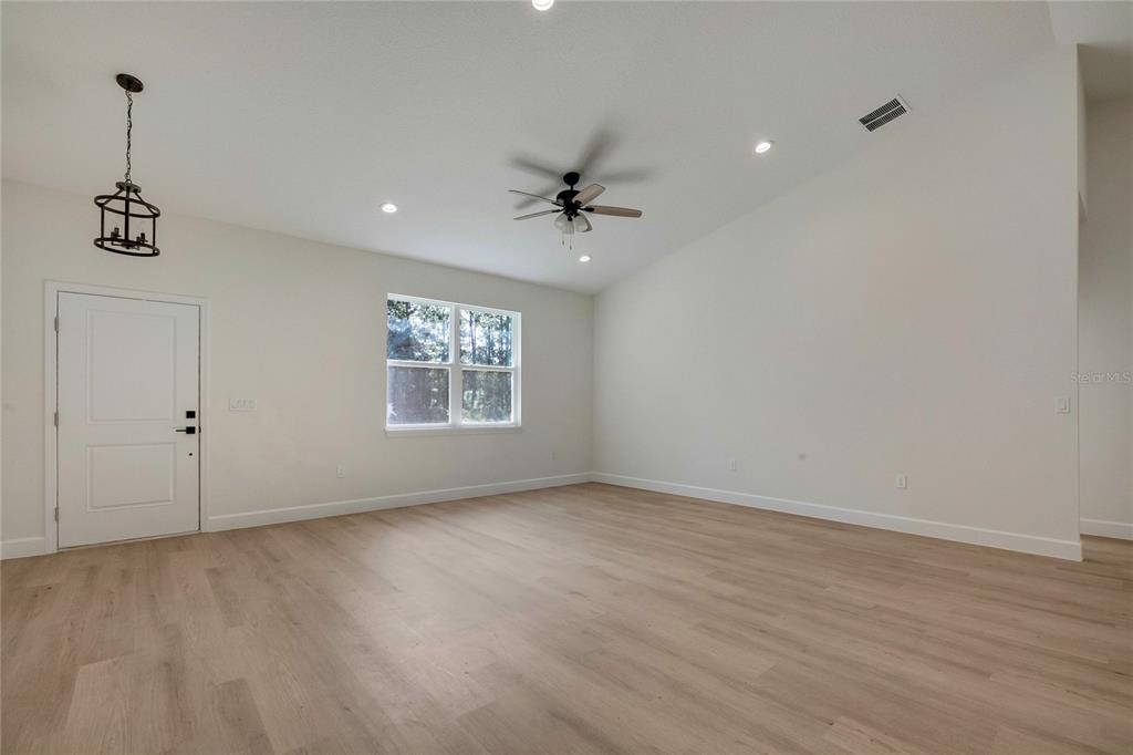 An empty living room features light wood-look flooring, white walls, a ceiling fan, and recessed lighting — 8104 N SANTOS DRIVE, CITRUS SPRINGS, FL