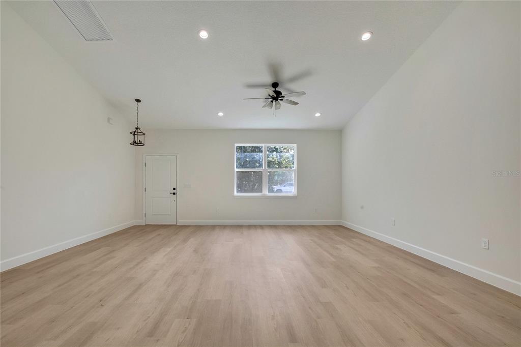 A spacious, empty room features light wood-look flooring, white walls, a ceiling fan, and recessed lighting — 8104 N SANTOS DRIVE, CITRUS SPRINGS, FL