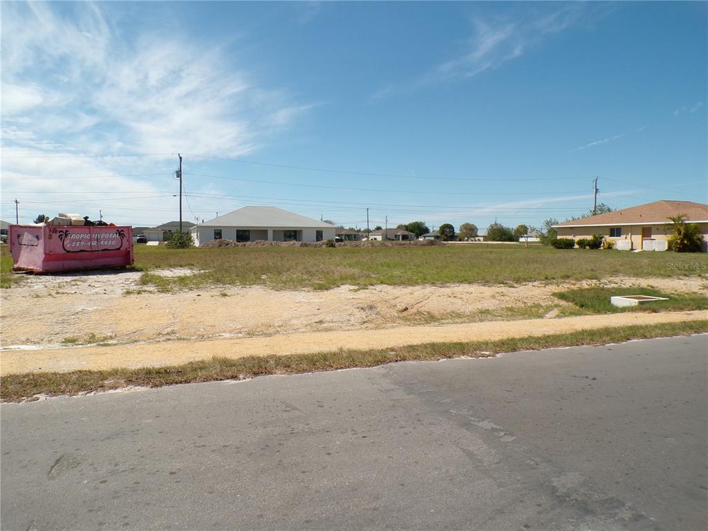 A vacant, grassy residential lot sits next to a pink dumpster under a blue sky — 1816 NE 8TH PLACE, CAPE CORAL, FL