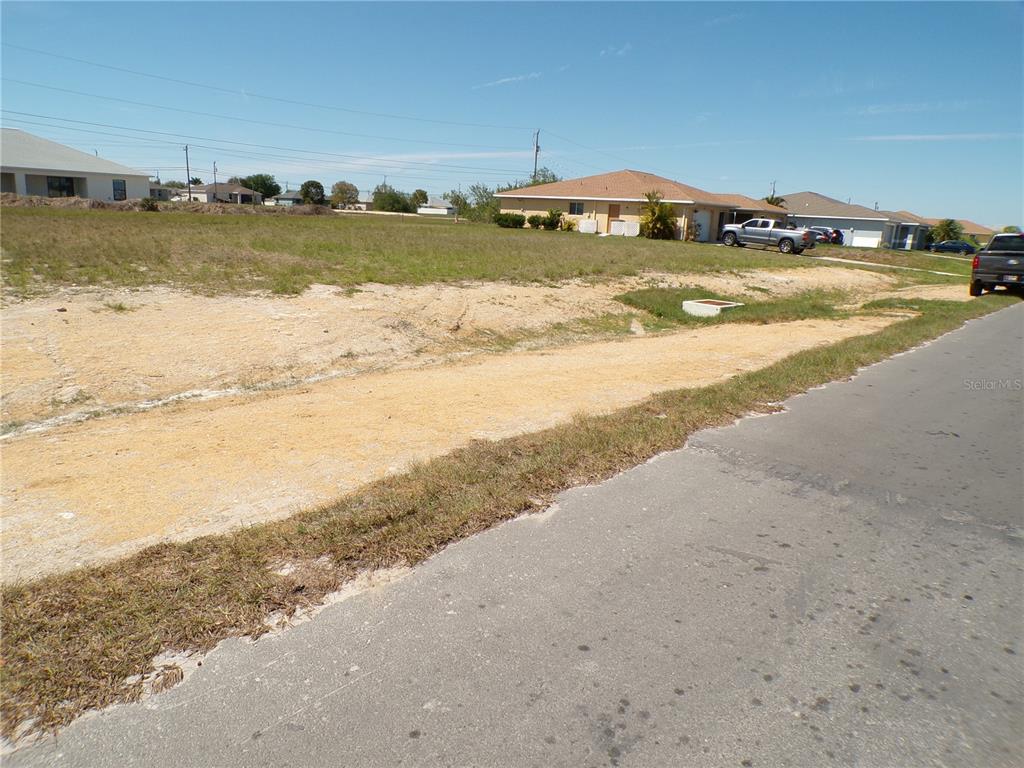 A vacant, grassy residential lot sits next to a paved road and neighboring houses — 1816 NE 8TH PLACE, CAPE CORAL, FL