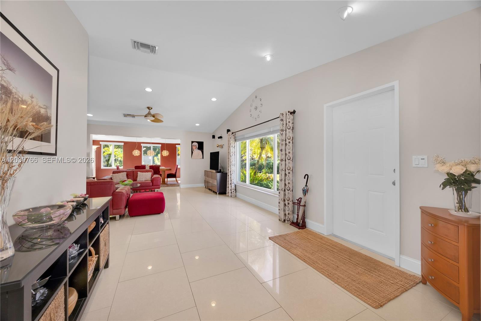 A bright, open-concept living area features light tile flooring, a vaulted ceiling, and a doorway — 11625 SW 70th Ave, Pinecrest FL 33156, PINECREST, FL
