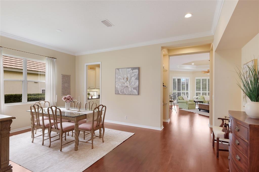 A dining room with a glass table and chairs leads into a living area beyond — 7241 ORCHID ISLAND PLACE, BRADENTON, FL