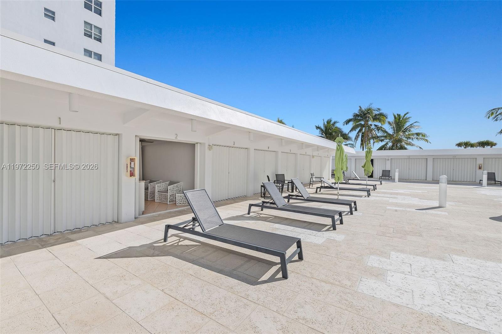 A row of beach cabanas features lounge chairs on a paved patio under a clear sky — 4925 Collins Ave, Miami Beach FL 33140, MIAMI BEACH, FL