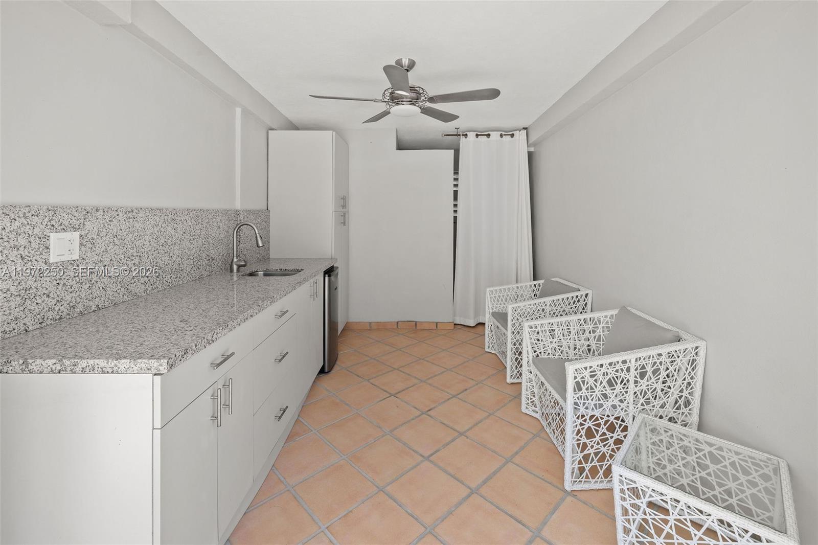 A kitchenette with granite countertops, white cabinets, and two white wicker chairs on tile flooring — 4925 Collins Ave, Miami Beach FL 33140, MIAMI BEACH, FL