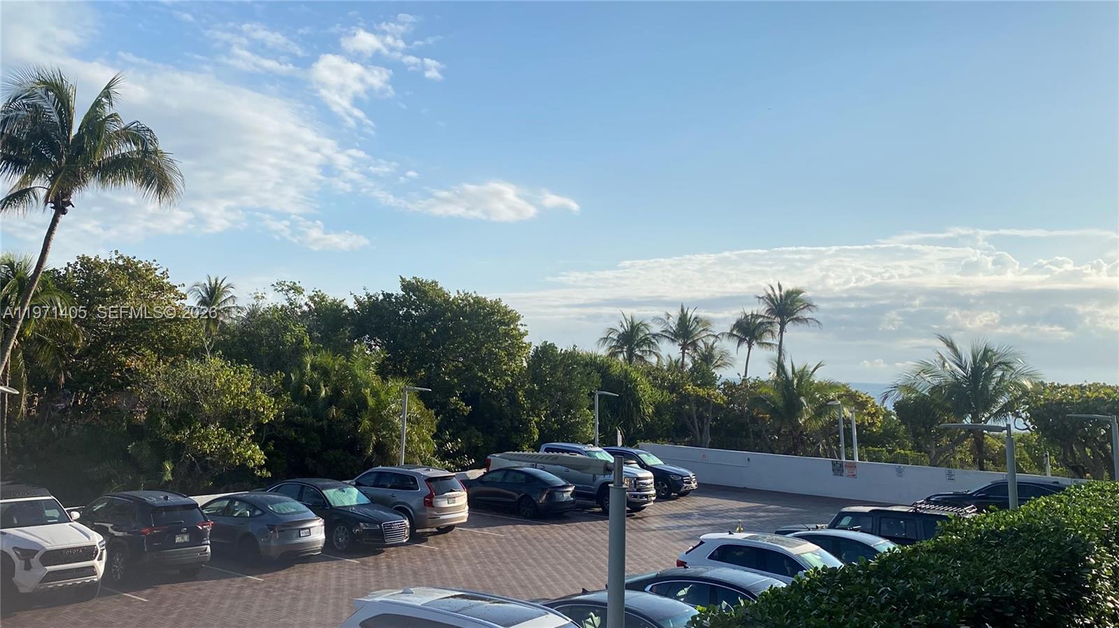A parking lot filled with various cars is surrounded by palm trees and lush greenery — 177 Ocean Lane Dr # 204, Key Biscayne FL 33149, KEY BISCAYNE, FL