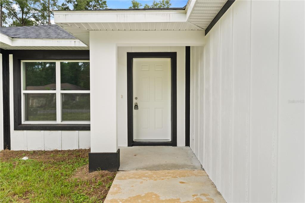 A white front door with black trim is set within a covered concrete entryway — 6026 NW 65TH STREET, OCALA, FL