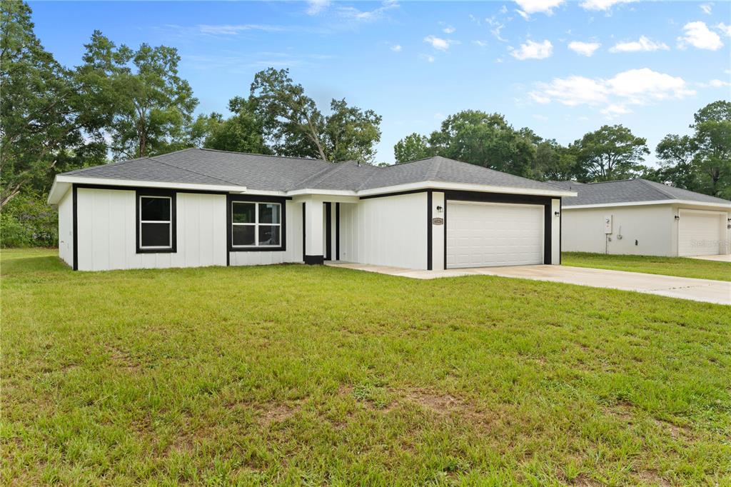 A single-story white house with black trim and a two-car garage sits on a lawn — 6026 NW 65TH STREET, OCALA, FL