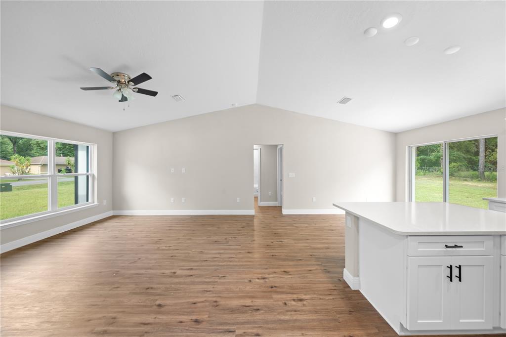 A spacious living room with vaulted ceilings, wood-look flooring, and a white kitchen island — 6026 NW 65TH STREET, OCALA, FL