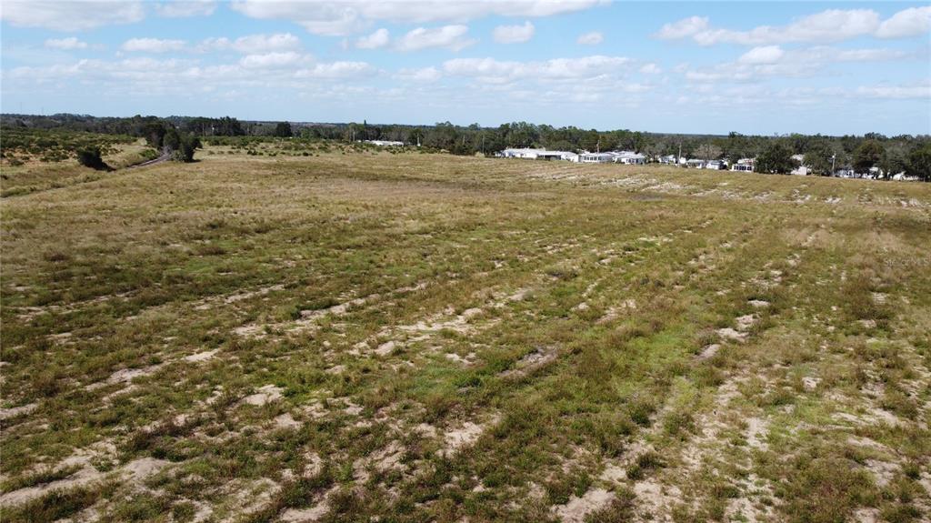 An aerial view shows a large, flat, grassy field with scattered trees and distant houses — 3200 POWER LINE ROAD, AVON PARK, FL