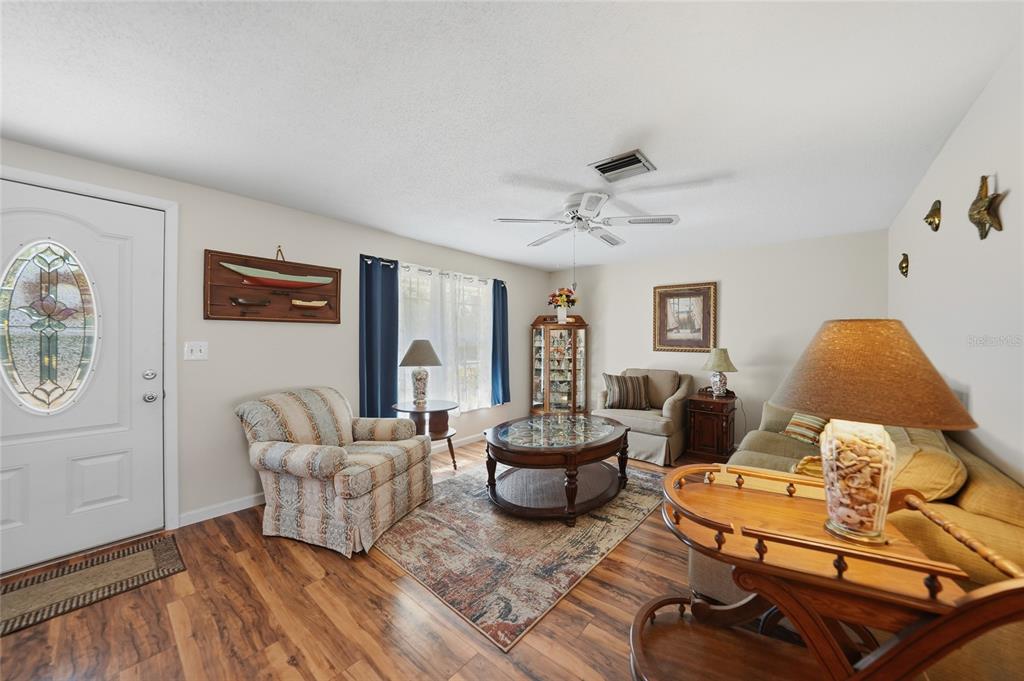A living room features wood-look flooring, a ceiling fan, a patterned rug, and furniture — 18366 BURKHOLDER CIRCLE, PORT CHARLOTTE, FL