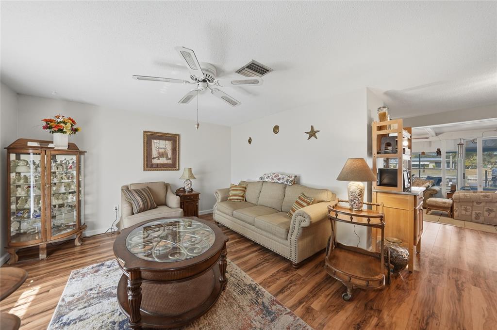 A living room features wood-look flooring, a beige sofa, a glass-topped coffee table, and cabinetry — 18366 BURKHOLDER CIRCLE, PORT CHARLOTTE, FL