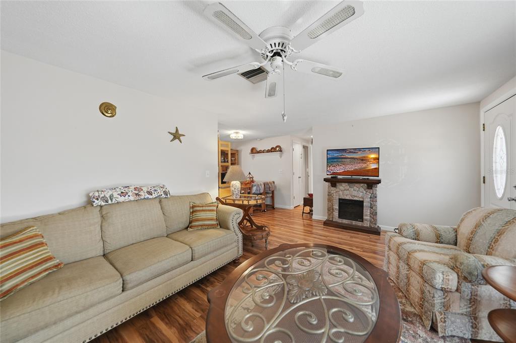 A living room features a beige sofa, patterned armchair, stone fireplace, and wood-look flooring — 18366 BURKHOLDER CIRCLE, PORT CHARLOTTE, FL