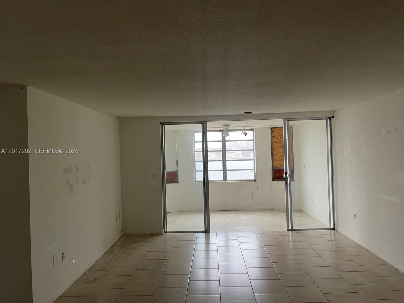 An interior view shows a tiled living area leading to a sunroom with sliding glass doors — 1660 NE 191st St # 1, Miami FL 33179, MIAMI, FL