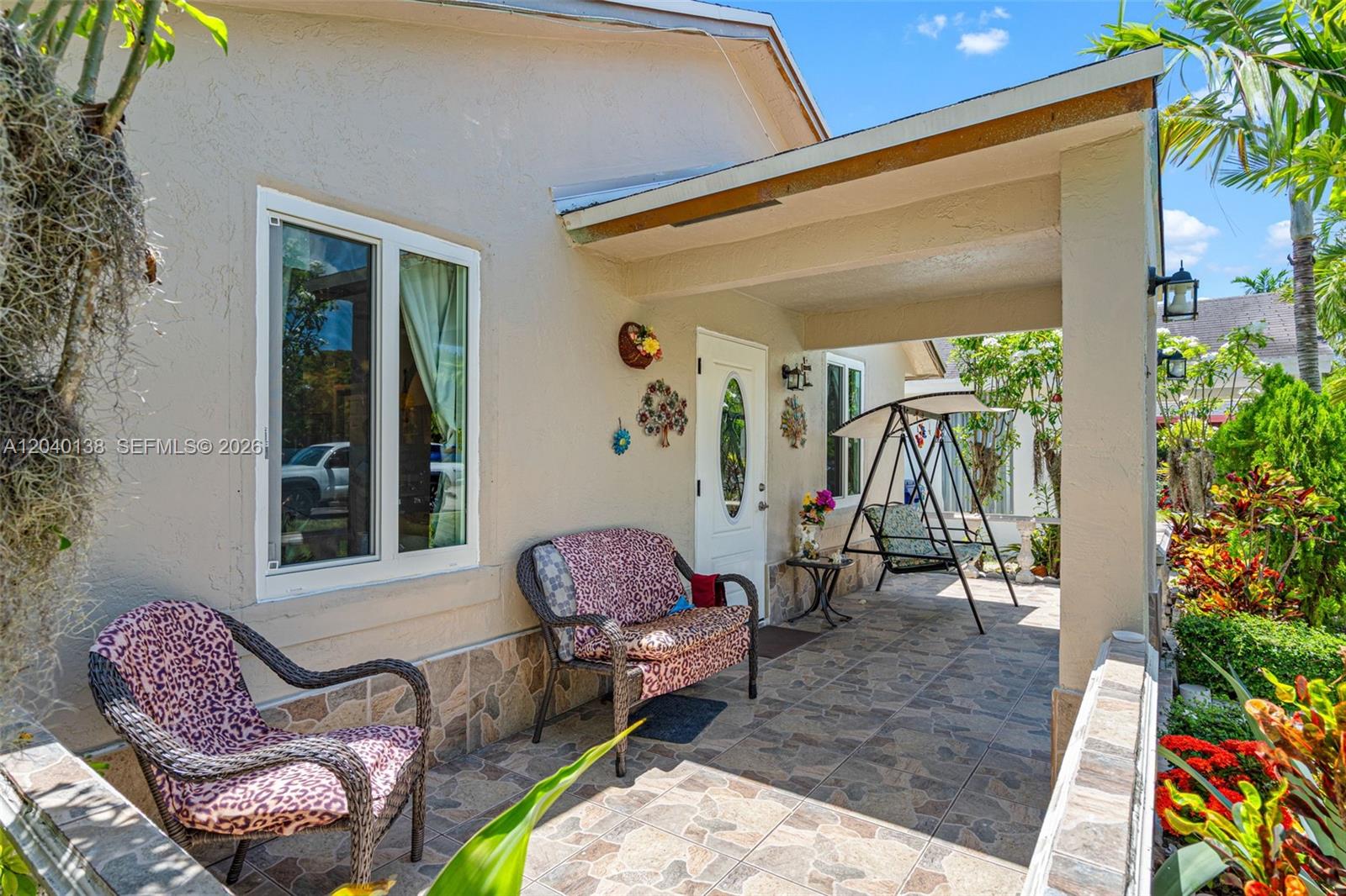 A covered patio features tiled flooring, wicker furniture with leopard-print cushions, and a porch swing — 12243 SW 201st Ter, Miami FL 33177, MIAMI, FL