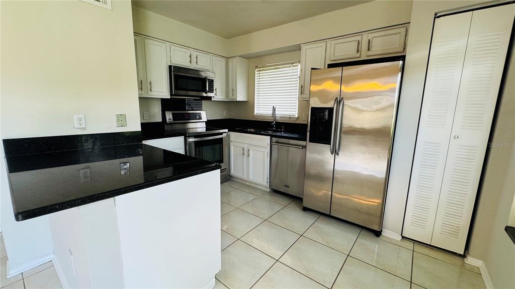 A kitchen features white cabinets, black countertops, stainless steel appliances, and light-colored floor tiles — 4415 PINEBARK AVENUE UNIT 48-4, ORLANDO, FL