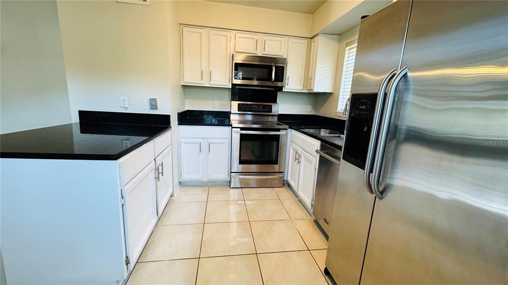 A kitchen features white cabinets, black countertops, stainless steel appliances, and light-colored tile flooring — 4415 PINEBARK AVENUE UNIT 48-4, ORLANDO, FL