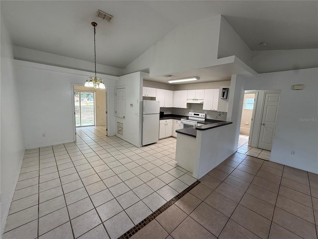 A kitchen with white cabinets and tile flooring opens into a dining area with a chandelier — 9515 SW 31ST COURT, OCALA, FL