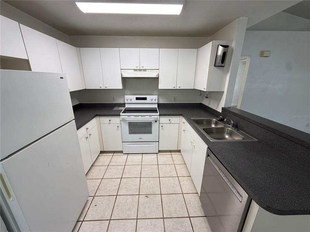 A kitchen features white cabinets, dark countertops, white appliances, and light-colored tiled flooring — 9515 SW 31ST COURT, OCALA, FL