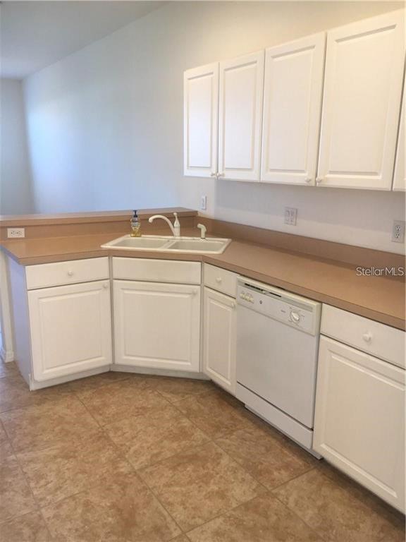 A kitchen features white cabinets, tan countertops, a double sink, and a white dishwasher — 4480 STREAMSIDE COURT UNIT 1505, SARASOTA, FL