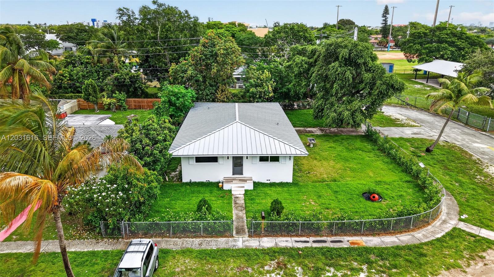 An aerial view shows a white single-story house with a metal roof and large yard — 1695 NE 160th St, North Miami Beach FL 33162, NORTH MIAMI BEACH, FL