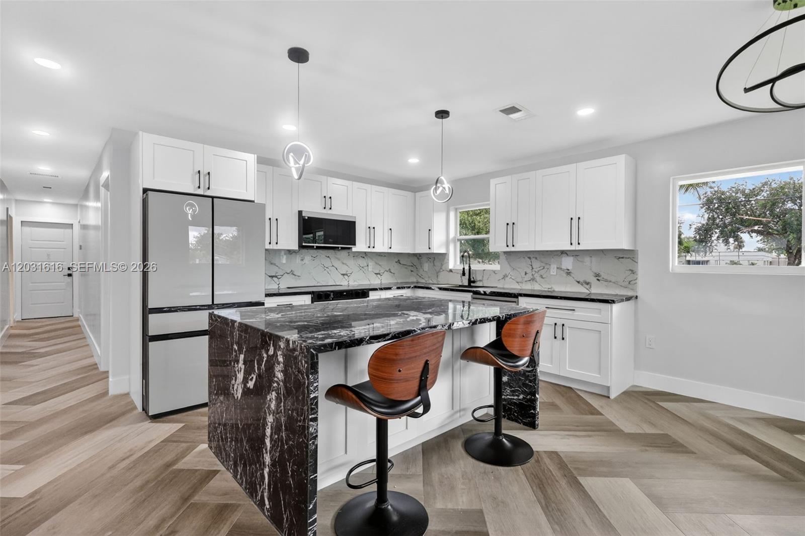 A modern kitchen features white cabinets, a black marble island, and chevron-patterned wood flooring — 1695 NE 160th St, North Miami Beach FL 33162, NORTH MIAMI BEACH, FL