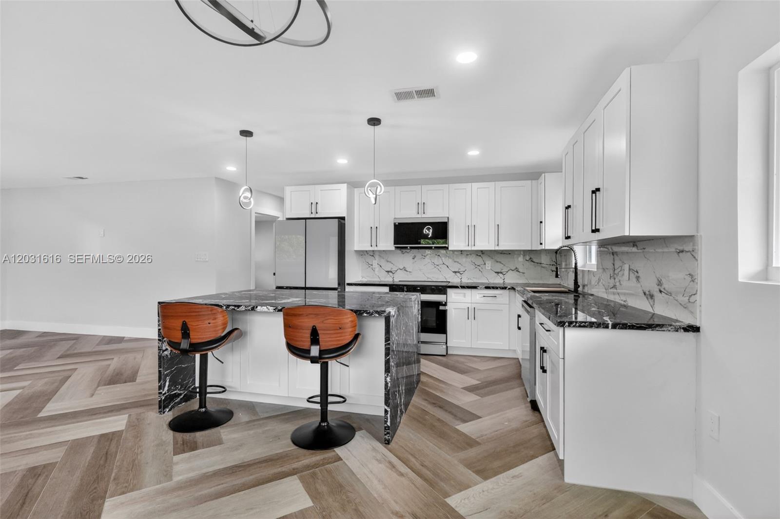 A modern kitchen features white cabinets, black marble countertops, and a herringbone wood floor — 1695 NE 160th St, North Miami Beach FL 33162, NORTH MIAMI BEACH, FL