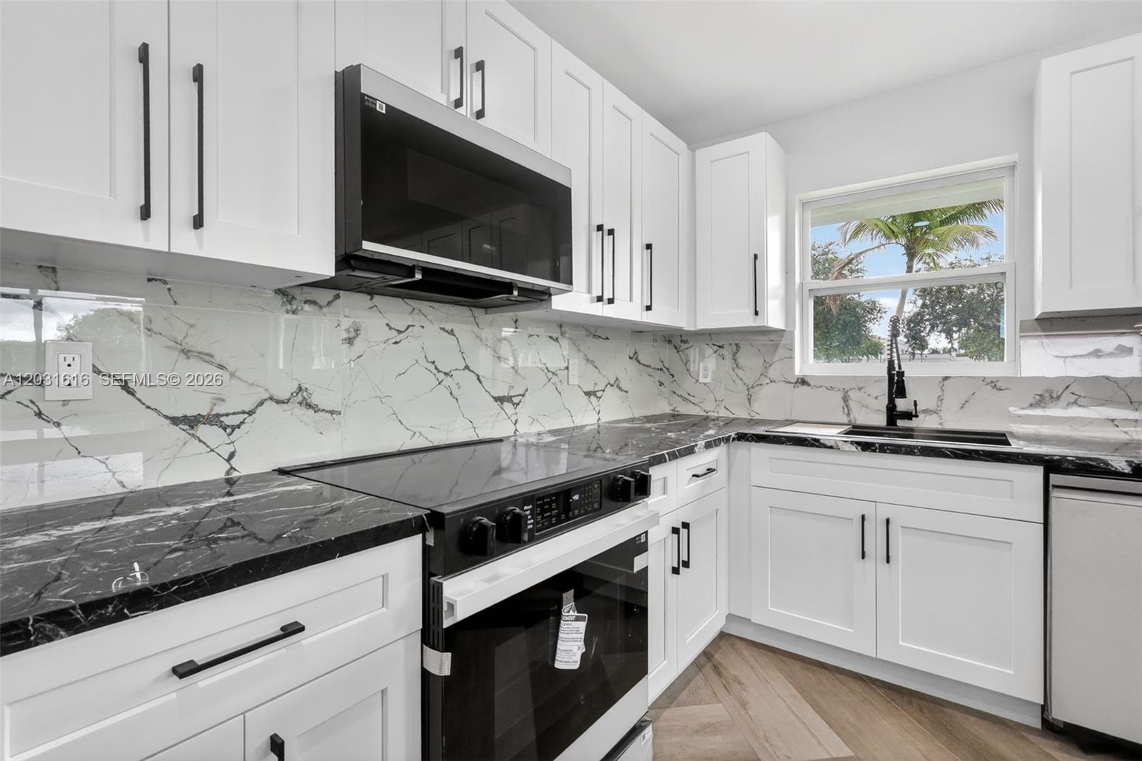A kitchen features white cabinets, black countertops, a marble-patterned backsplash, and stainless steel appliances — 1695 NE 160th St, North Miami Beach FL 33162, NORTH MIAMI BEACH, FL