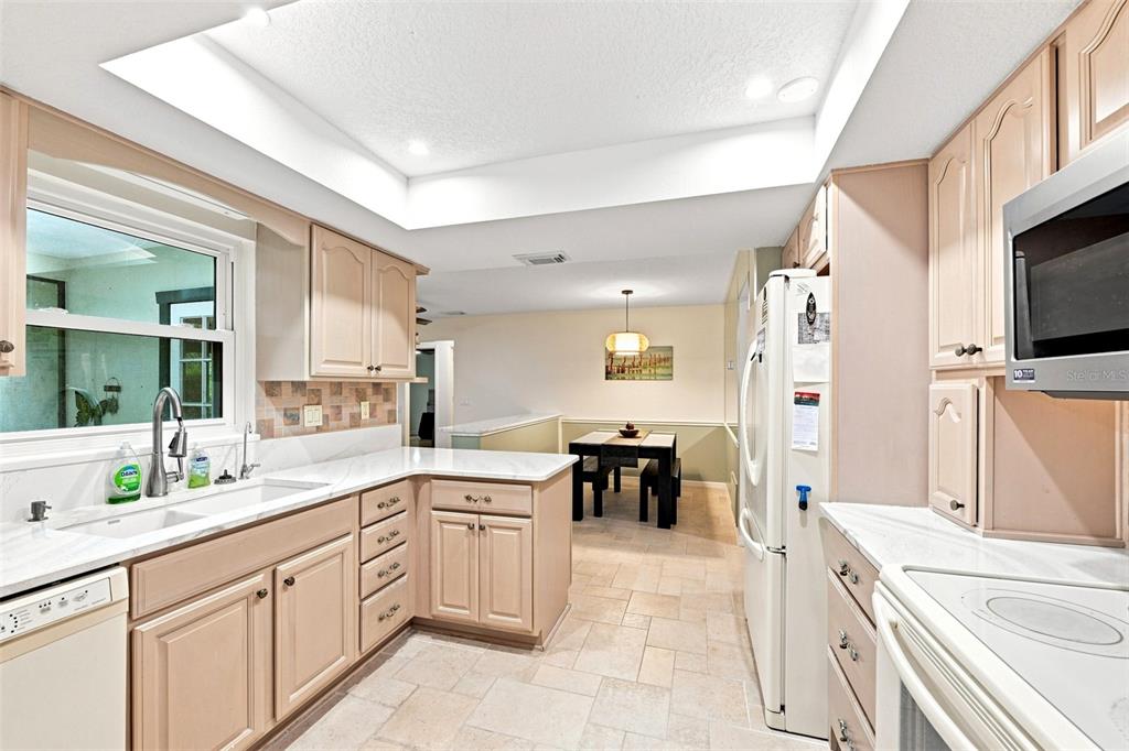 A kitchen features light wood cabinets, white countertops, a tile backsplash, and an adjacent dining area — 2107 W FORE DRIVE, TAMPA, FL