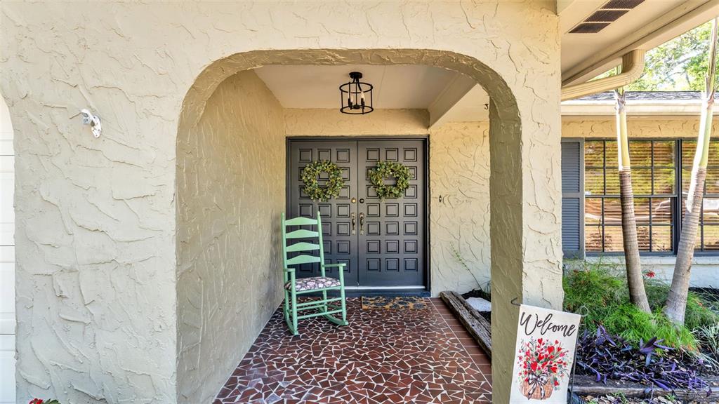 A covered entryway features a tiled floor, a green rocking chair, and double front doors — 6321 FERN LANE, LAKELAND, FL