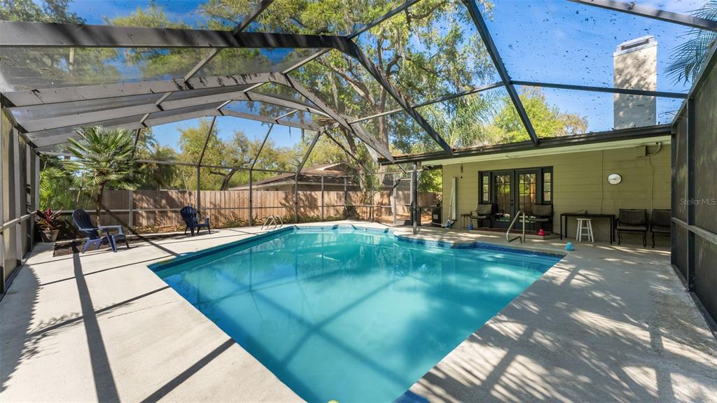 A screened-in swimming pool with a concrete deck sits behind a house with a chimney — 6321 FERN LANE, LAKELAND, FL