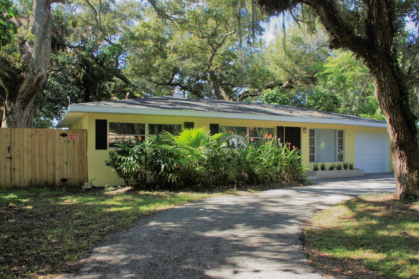 A yellow single-story house with a driveway, a wooden fence, and mature trees — 635 18th Place, Vero Beach FL 32960, VERO BEACH, FL