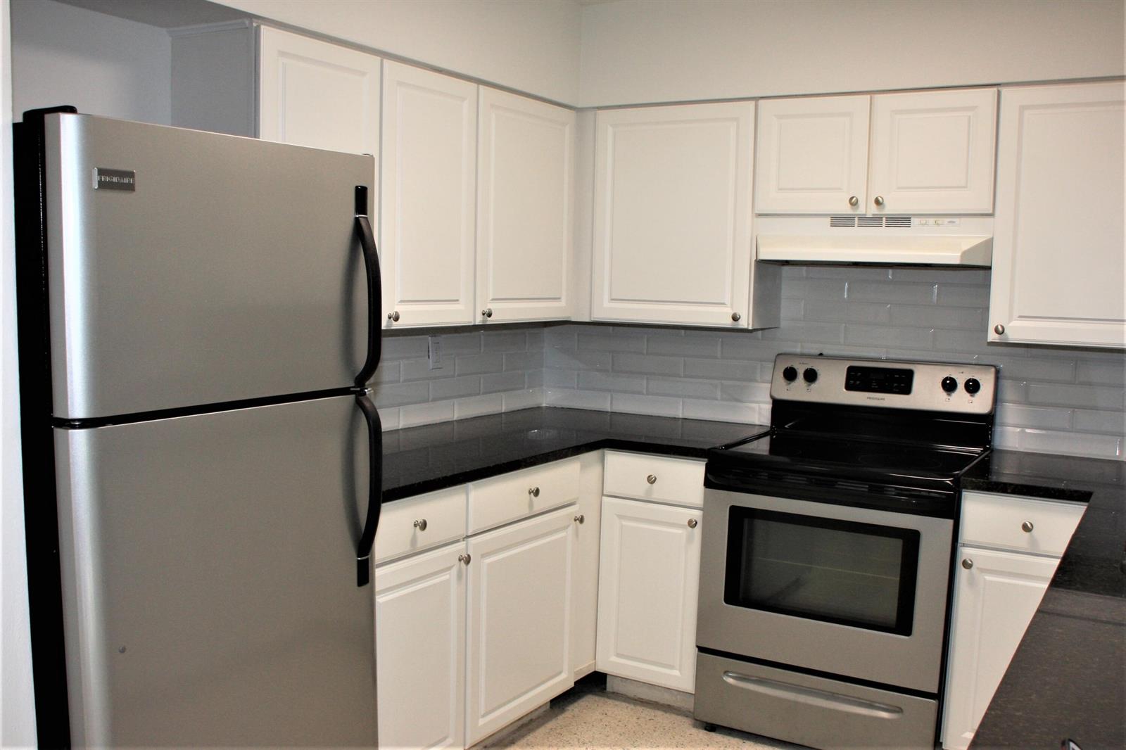 A kitchen with white cabinets, black countertops, stainless steel appliances, and a gray subway tile backsplash — 635 18th Place, Vero Beach FL 32960, VERO BEACH, FL
