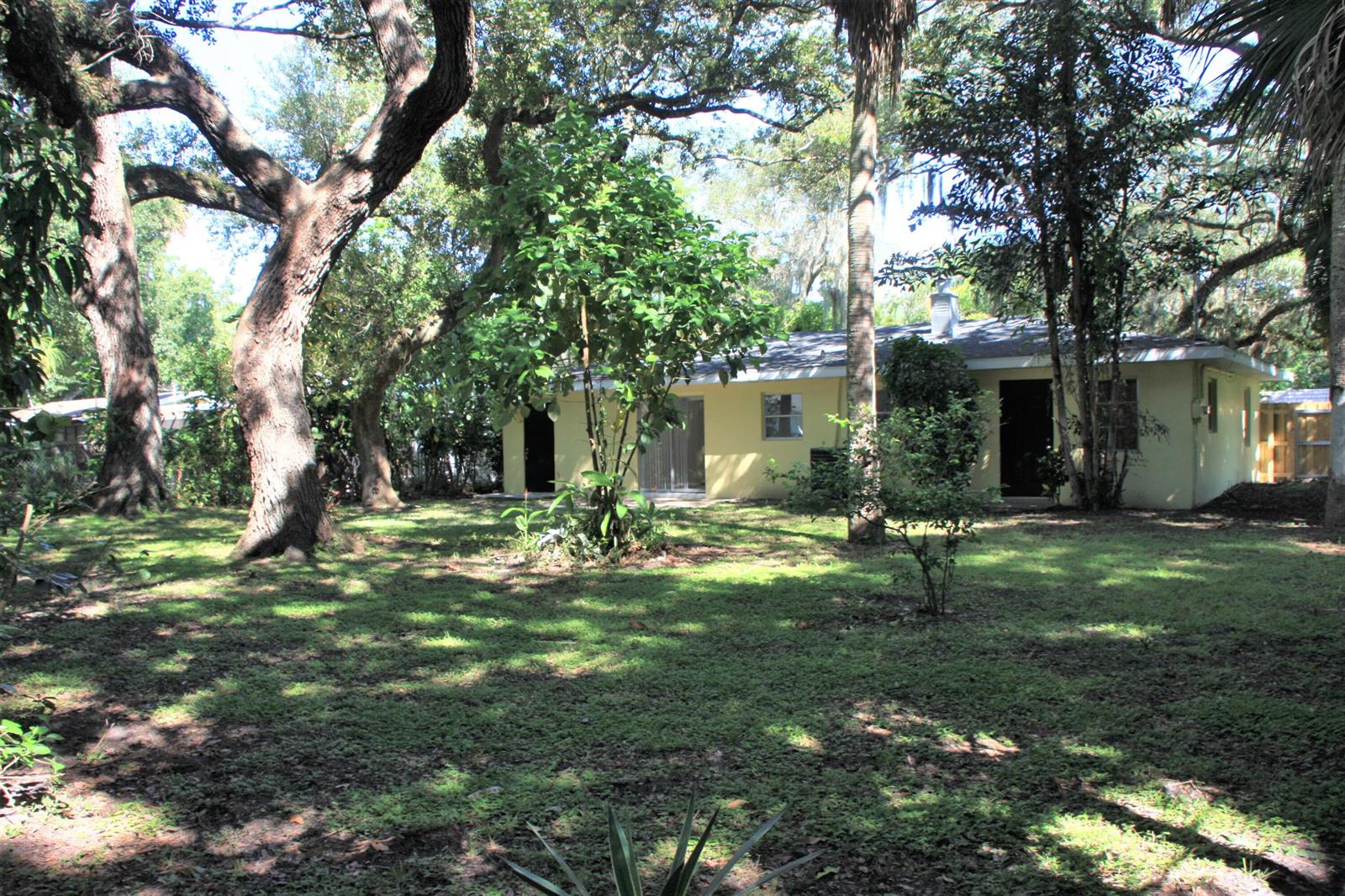 A yellow single-story house sits in a grassy, tree-shaded backyard — 635 18th Place, Vero Beach FL 32960, VERO BEACH, FL
