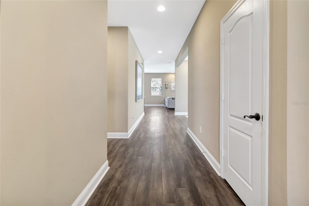 A hallway with wood-look flooring leads toward an open living area with a white door — 549 CHAMPION RIDGE DRIVE, DAYTONA BEACH, FL