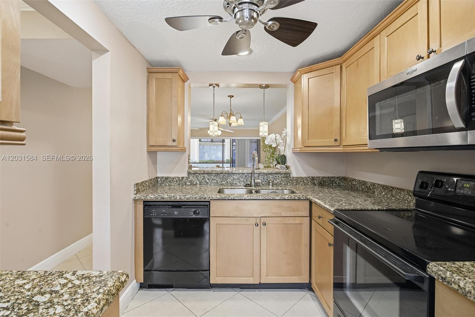 A kitchen features light wood cabinets, granite countertops, black appliances, and a ceiling fan — 2379 SW 15th St # 107, Deerfield Beach FL 33442, DEERFIELD BEACH, FL