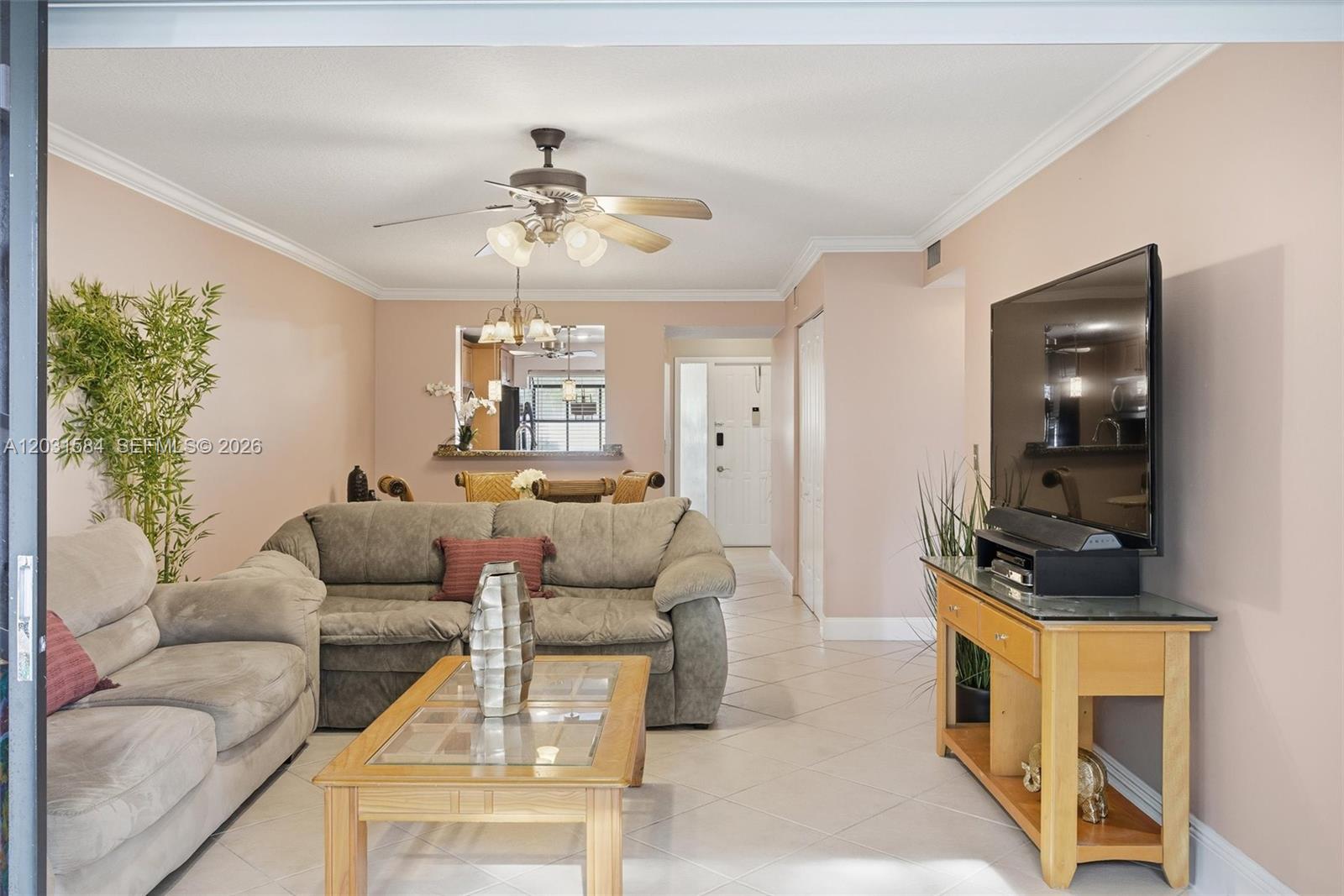 This living room features light-colored tile flooring, a ceiling fan, and a wall-mounted television — 2379 SW 15th St # 107, Deerfield Beach FL 33442, DEERFIELD BEACH, FL