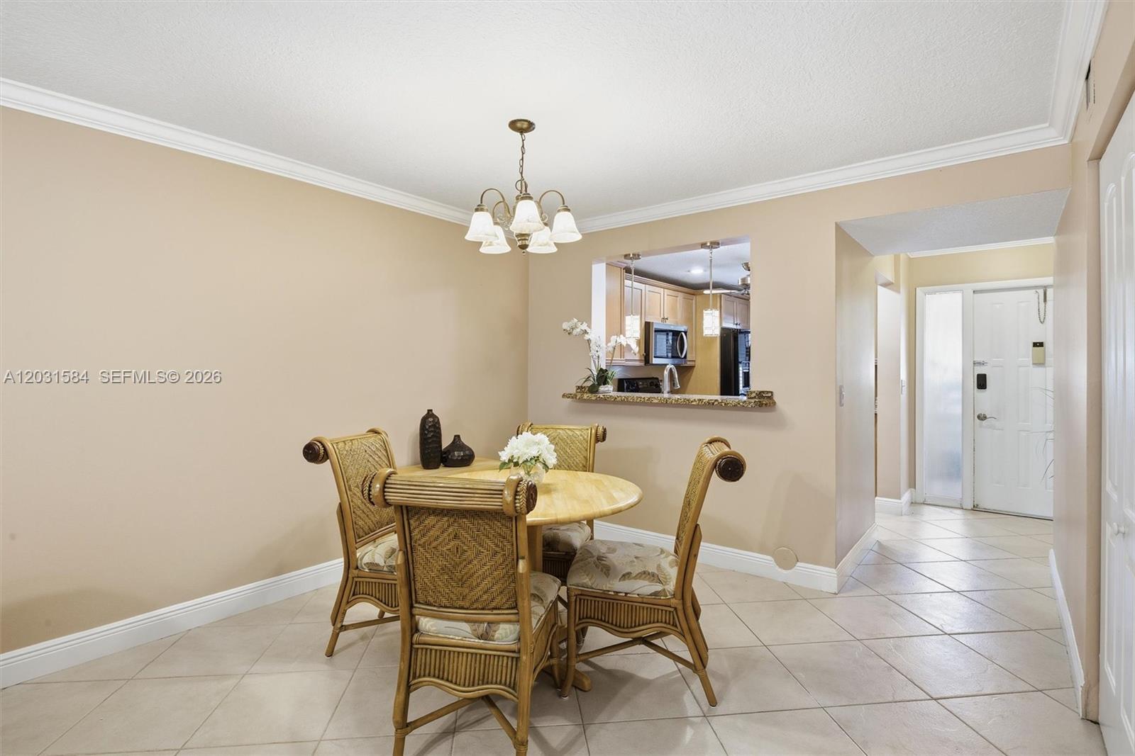 A dining area features a round wooden table with four rattan chairs and tile flooring — 2379 SW 15th St # 107, Deerfield Beach FL 33442, DEERFIELD BEACH, FL