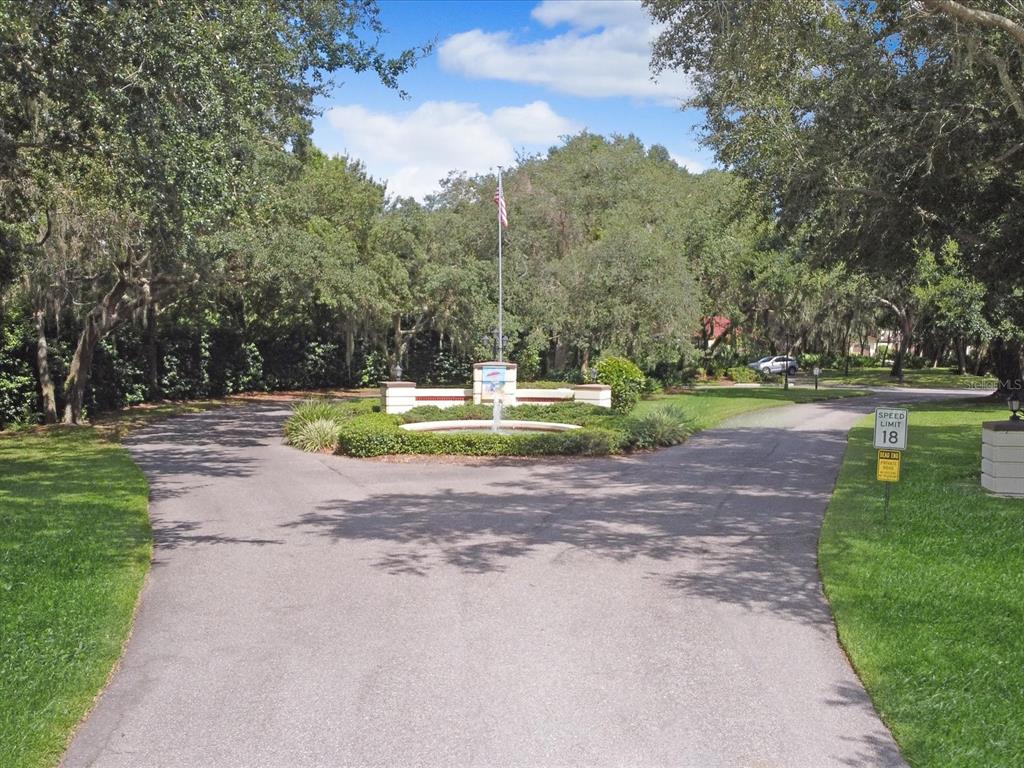 A paved driveway splits around a central fountain and flagpole in a wooded residential area — 159 COVENTRY CIRCLE, HAINES CITY, FL
