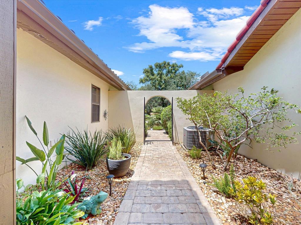 A stone walkway leads through a courtyard between two stucco walls toward an arched gate — 159 COVENTRY CIRCLE, HAINES CITY, FL