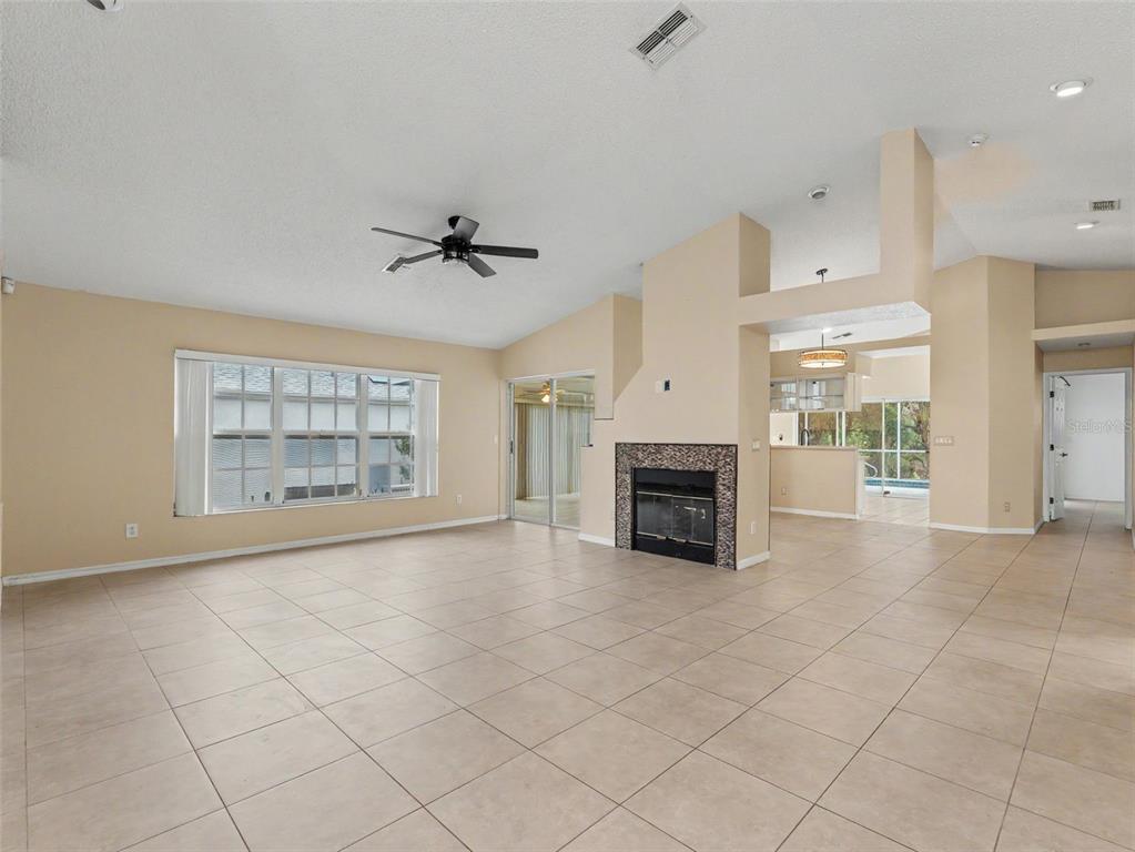 A spacious living room features light tile flooring, a fireplace, and a ceiling fan — 10439 CASA GRANDE CIRCLE, SPRING HILL, FL